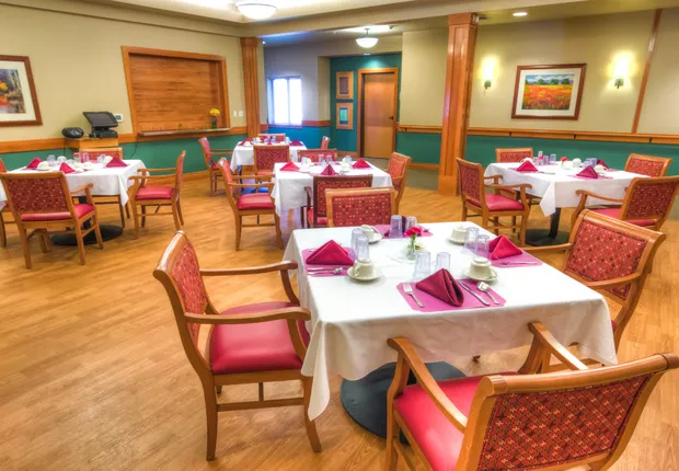 Senior Living community in Vancouver featuring a dining hall with white table clothes and red chairs.