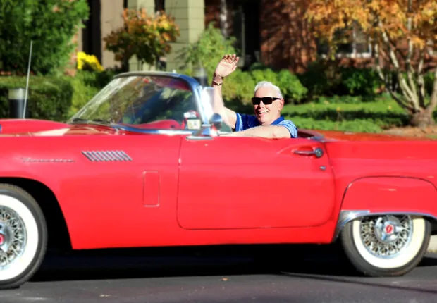 A cool senior man in sunglasses shows off his red convertible.