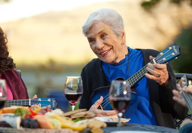 Senior woman playing the ukulele to her friends over dinner.