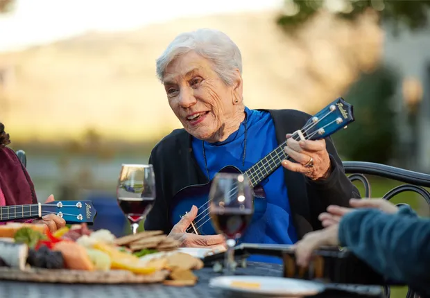 Senior woman playing the ukulele for her friends over wine.