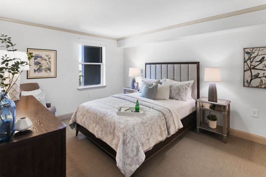 model bedroom with white bed sheets and grey headboard in a white room