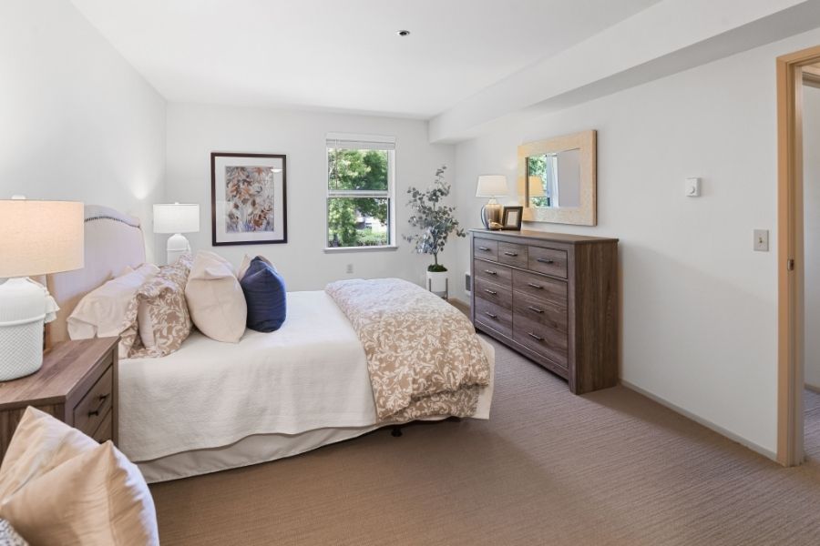 side view of model bedroom with white bedsheets and a brown dresser