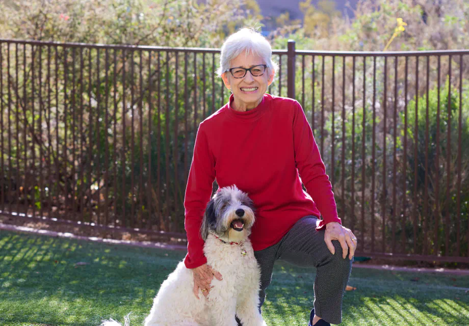 A senior woman in a red sweater posing with her dog.