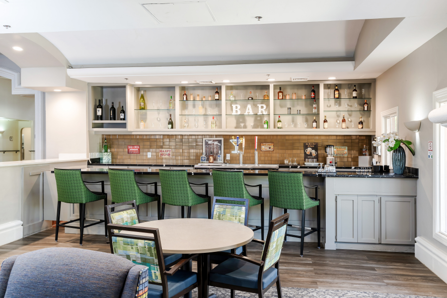 Close-up of the stylish bar area with green chairs and a modern display of beverages at Park Terrace Senior Living in Phoenix, AZ.