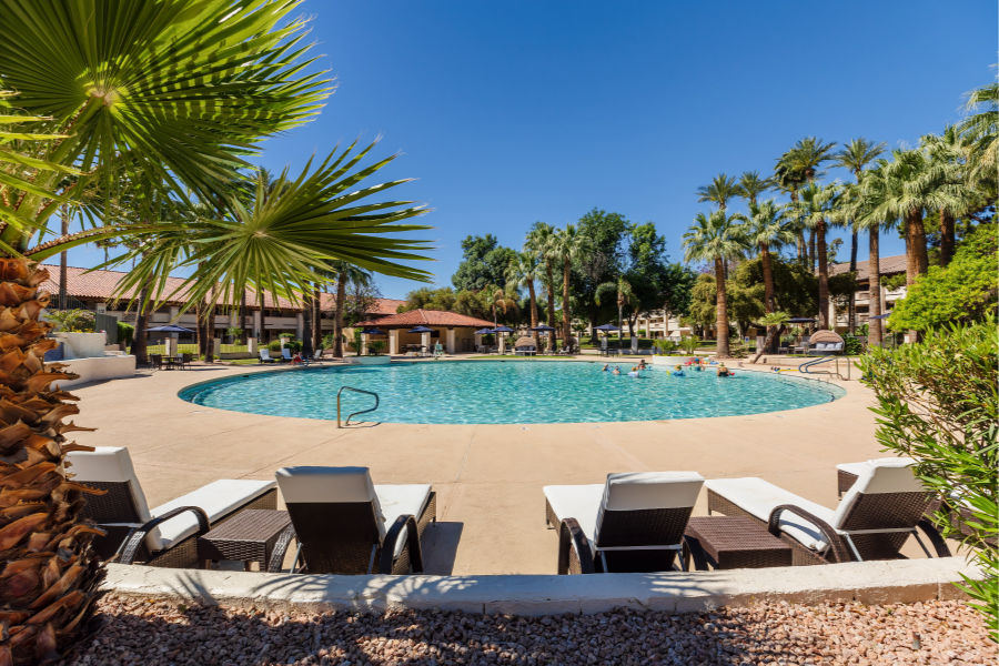 Comfortable lounge chairs by the outdoor pool at Park Terrace Senior Living in Phoenix, AZ, with palm trees and clear skies in the background.