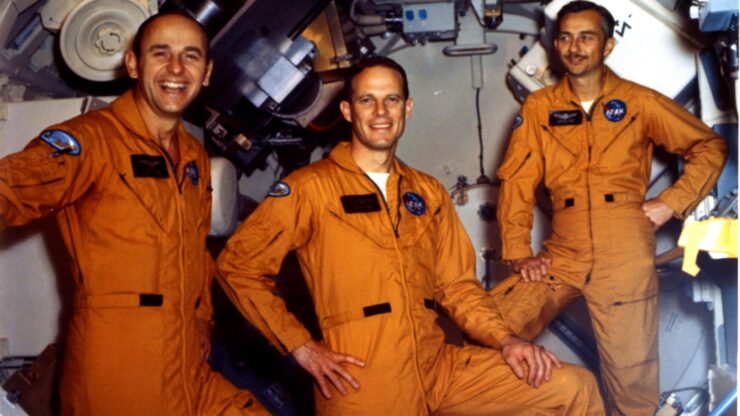 Three cheerful astronauts in orange jumpsuits exude camaraderie and excitement in a vibrant, high-tech setting.