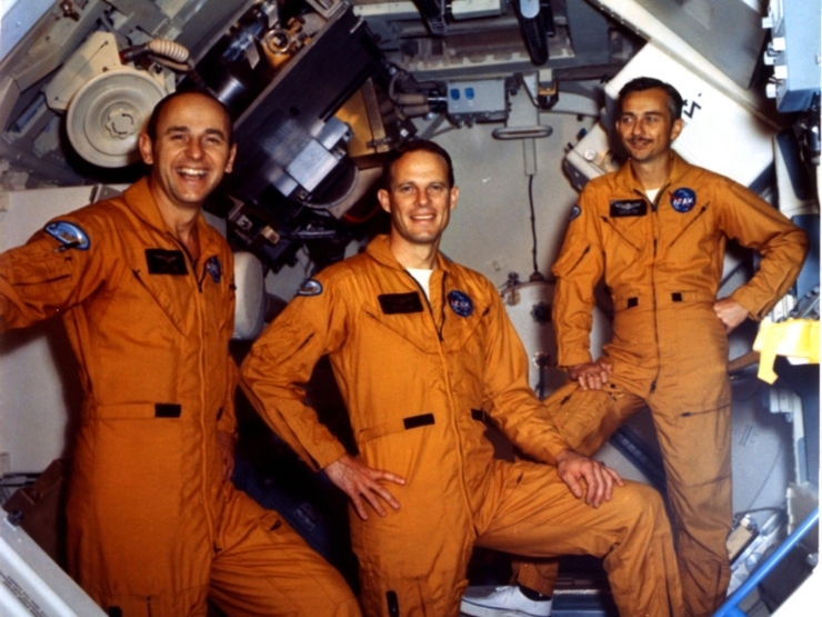 Three cheerful astronauts in orange jumpsuits exude camaraderie and excitement in a vibrant, high-tech setting.