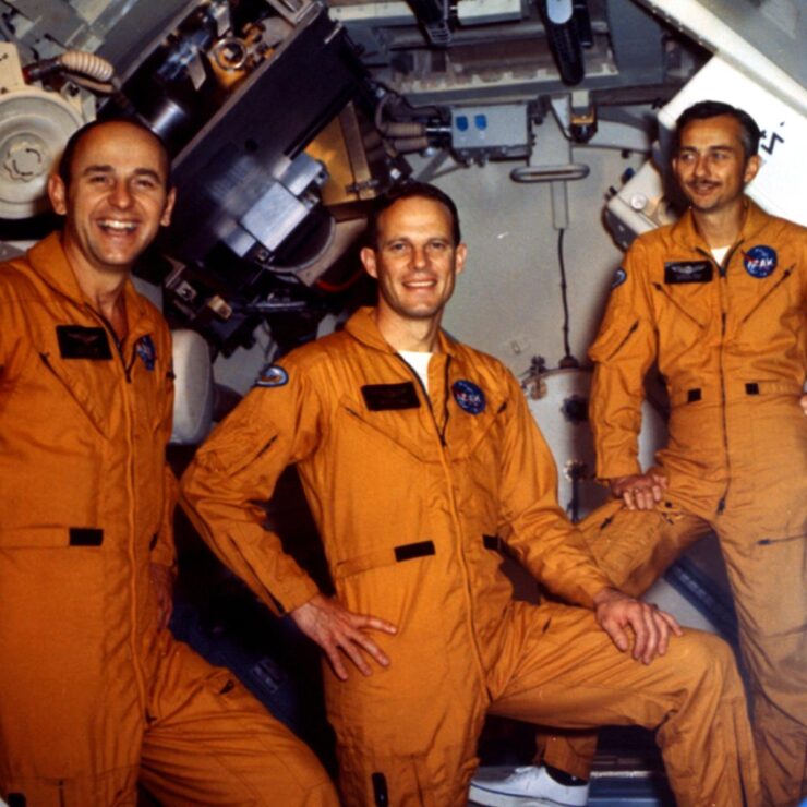 Three cheerful astronauts in orange jumpsuits exude camaraderie and excitement in a vibrant, high-tech setting.