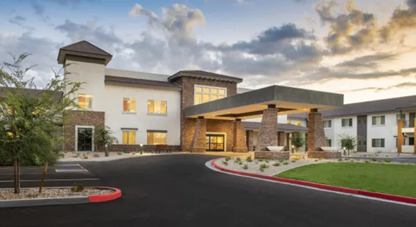 A welcoming retirement community with beautiful architecture, lush landscaping, and warm lighting.