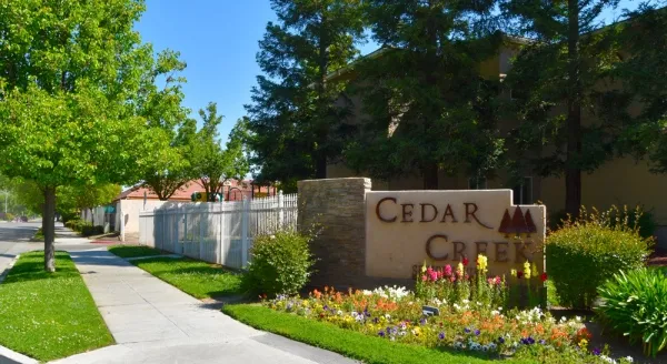 Welcoming entrance to Cedar Creek, surrounded by vibrant gardens and lush greenery, perfect for community living.