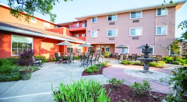 A sunny courtyard with inviting seating, lush greenery, and a tranquil fountain fosters community and connection.