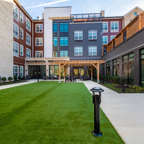 A welcoming courtyard with lush greenery, inviting seating, and bright, modern architecture fosters community warmth.