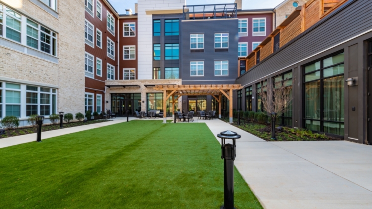 A welcoming courtyard with lush greenery, inviting seating, and bright, modern architecture fosters community warmth.