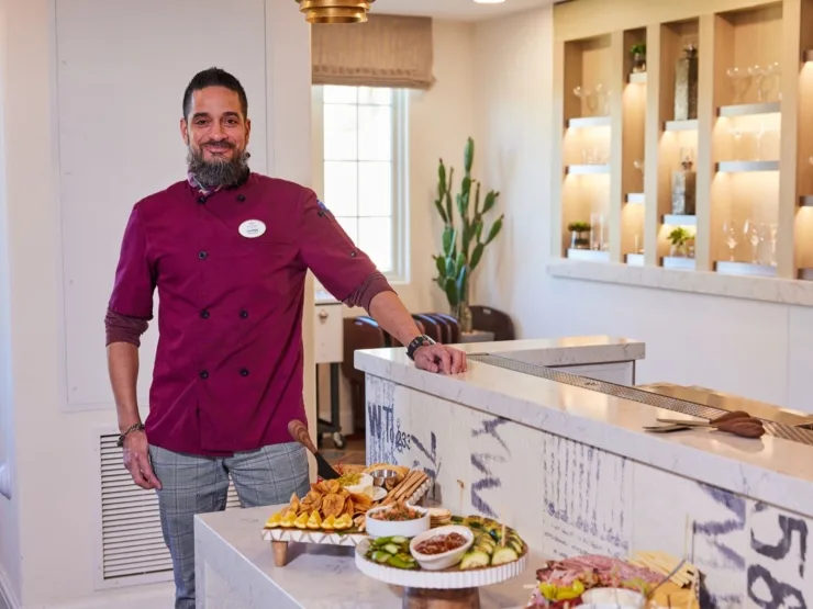 A welcoming chef stands proudly beside a beautifully arranged food spread, enhancing community warmth.