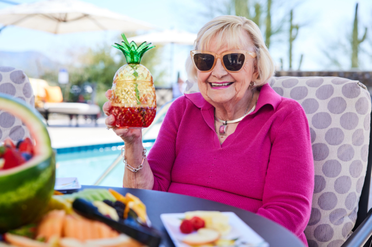 A joyful resident enjoys a refreshing drink by the pool, surrounded by vibrant fruit platters, radiating community warmth.