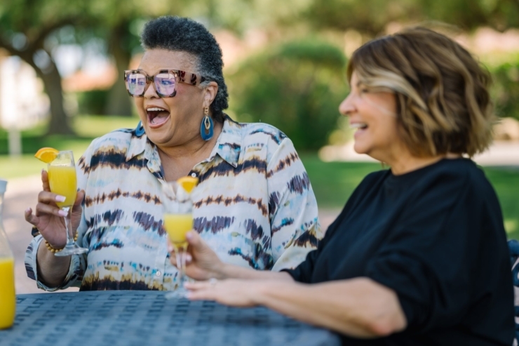 Laughter and joy fill the air as two friends enjoy refreshing drinks together in a sunny garden setting.