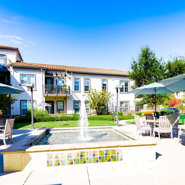 A sunny courtyard featuring cozy seating, a tranquil fountain, and vibrant gardens, inviting community connections.