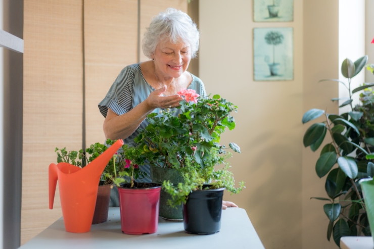 A smiling woman cares for vibrant flowers, surrounded by greenery, fostering a nurturing community atmosphere.