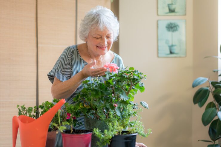 A smiling woman cares for vibrant flowers, surrounded by greenery, fostering a nurturing community atmosphere.
