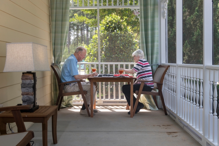 Two residents enjoy a pleasant afternoon playing a game together on a screened porch, surrounded by nature.