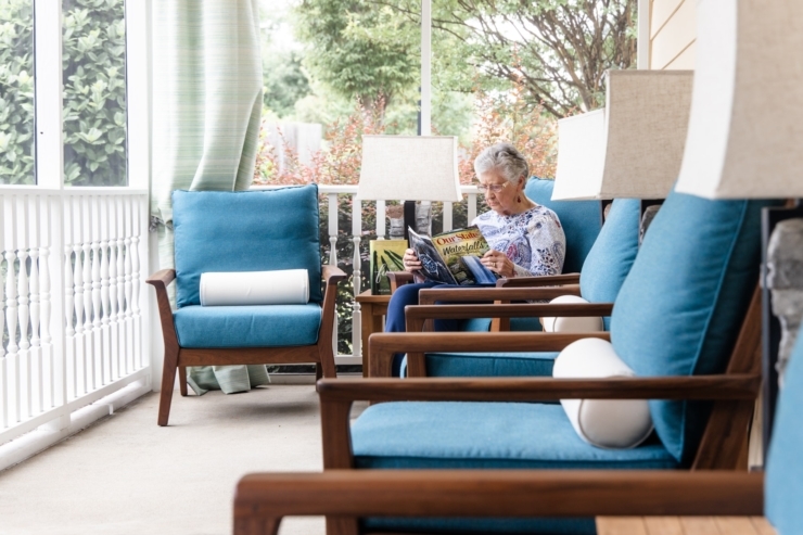 A serene porch setting, featuring a resident enjoying a magazine amidst cozy seating and natural light.