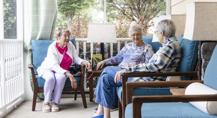 Three residents enjoy warm conversation on a sunny porch, fostering community and connection.