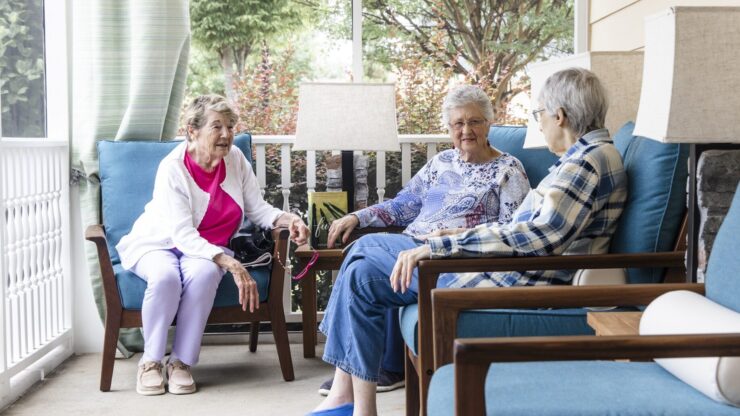 Three residents enjoy warm conversation on a sunny porch, fostering community and connection.