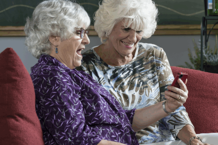Two cheerful women share a joyful moment on a cozy couch, enjoying each other's company and laughter.