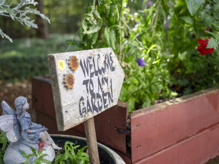 A charming garden scene invites warmth and community, featuring a whimsical sign and vibrant plants.