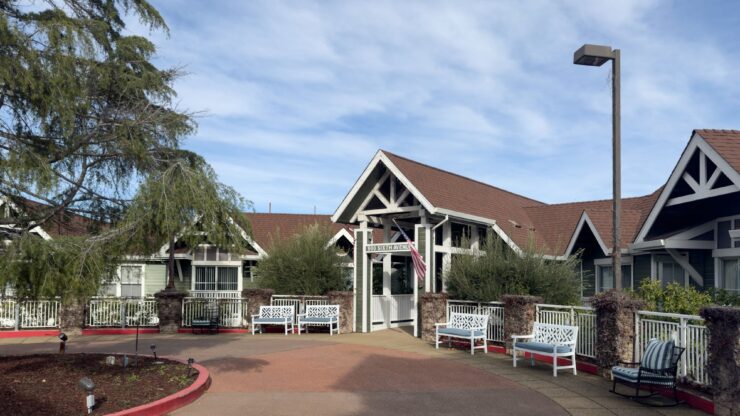 A welcoming entrance with cozy seating, surrounded by greenery and a bright, sunny sky.
