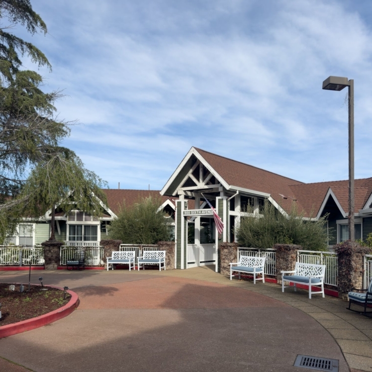 A welcoming entrance with cozy seating, surrounded by greenery and a bright, sunny sky.