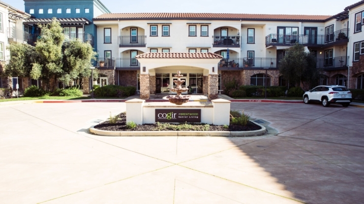 A welcoming community entrance features a charming fountain, surrounded by lush greenery and vibrant buildings.