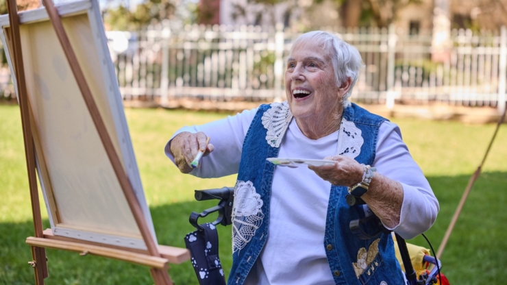 A joyful resident paints outdoors, surrounded by greenery, embodying warmth and community spirit.