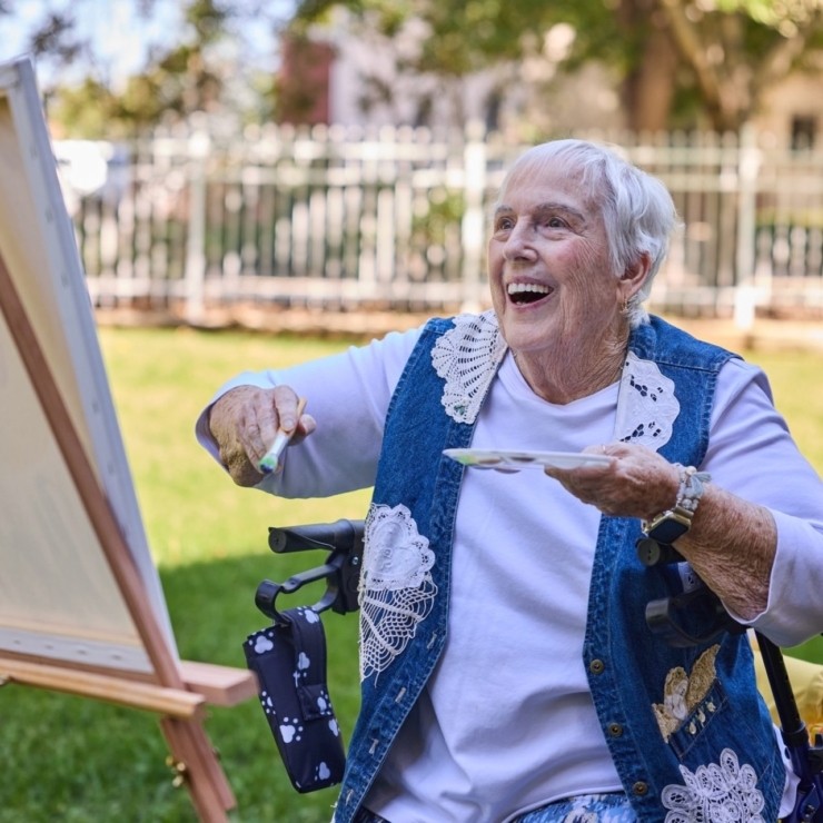 A joyful resident paints outdoors, surrounded by greenery, embodying warmth and community spirit.