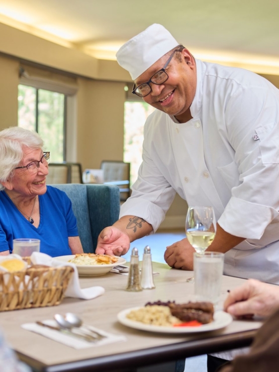 A warm dining scene with smiling residents enjoying a meal, fostered by attentive service in a vibrant setting.