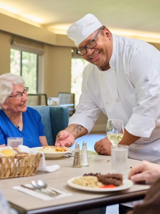 A warm dining scene with smiling residents enjoying a meal, fostered by attentive service in a vibrant setting.