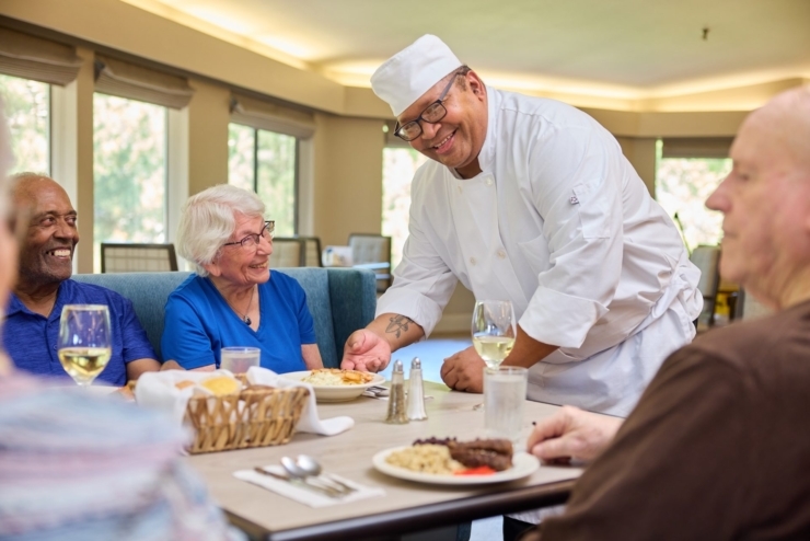 A warm dining scene with smiling residents enjoying a meal, fostered by attentive service in a vibrant setting.
