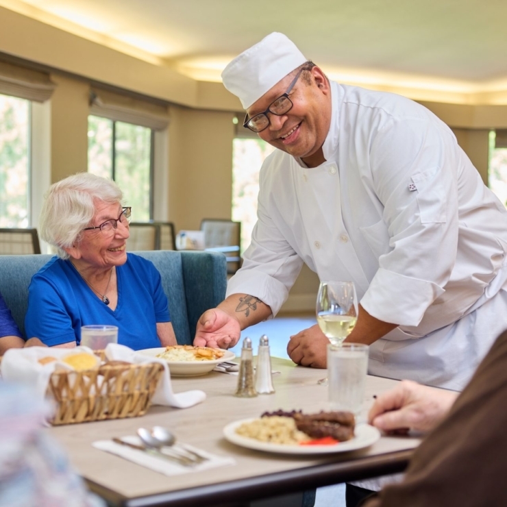 A warm dining scene with smiling residents enjoying a meal, fostered by attentive service in a vibrant setting.