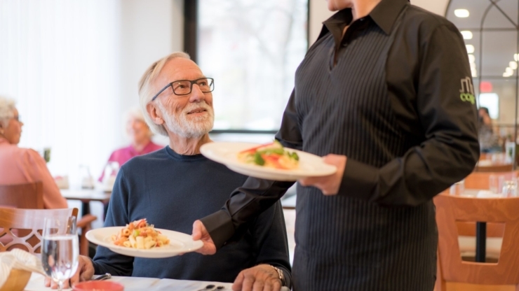 A cheerful dining scene where a resident enjoys a meal served with care and attention in a warm community atmosphere.