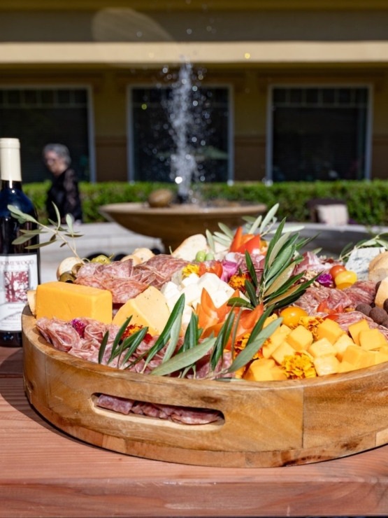 A beautifully arranged platter of wine, cheeses, and charcuterie invites warmth and community, showcasing a vibrant outdoor gathering.