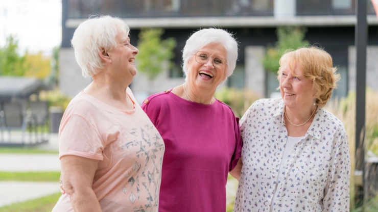 Three smiling women enjoy a joyful moment outdoors, embodying warmth and community spirit.