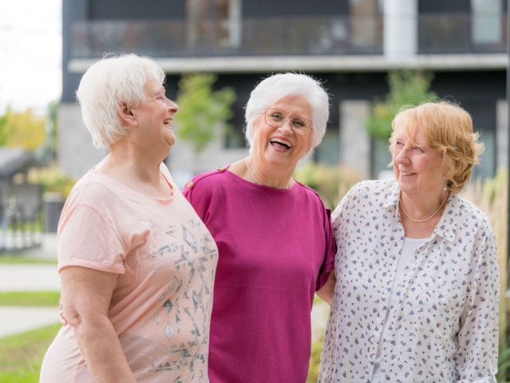Three smiling women enjoy a joyful moment outdoors, embodying warmth and community spirit.
