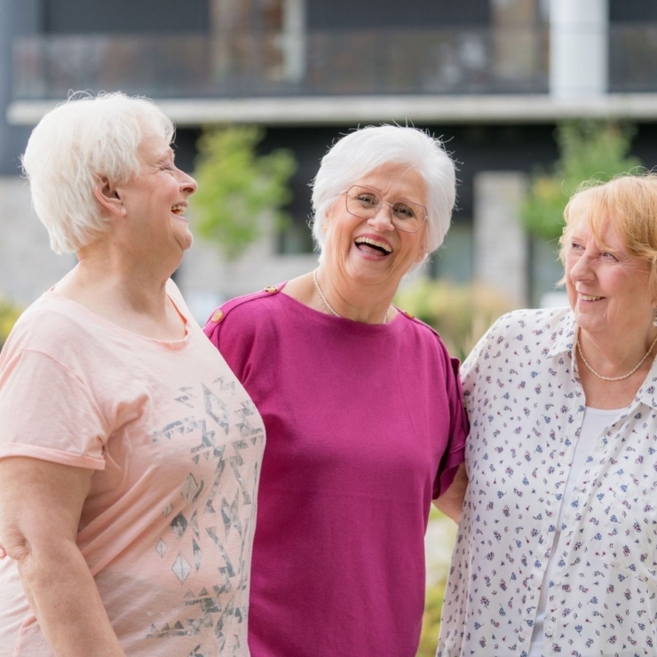 Three smiling women enjoy a joyful moment outdoors, embodying warmth and community spirit.
