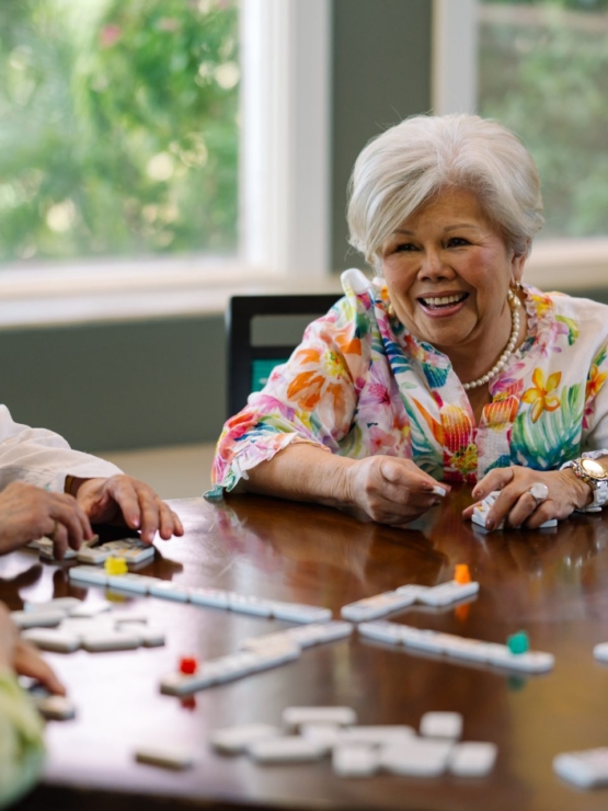 Engaged residents share laughter and friendship while enjoying a lively game around a sunlit table.