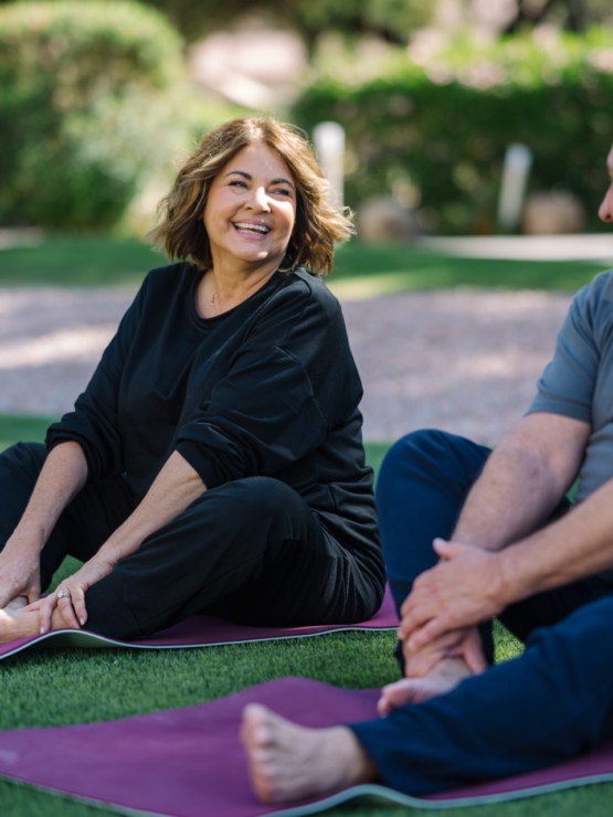 Two residents share a joyful moment on yoga mats in a vibrant, green outdoor setting, radiating community spirit.