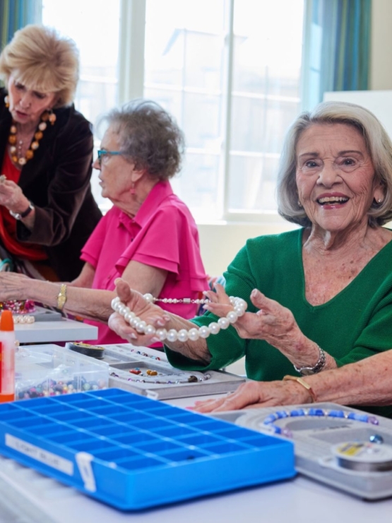 Residents joyfully create beautiful jewelry together, fostering friendship and creativity in a bright space.
