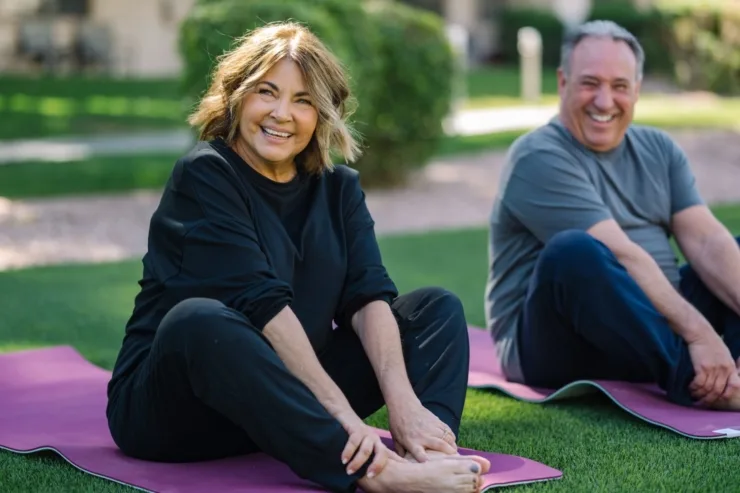 Lively individuals engage in yoga on vibrant mats, surrounded by greenery, sharing joy and connection.