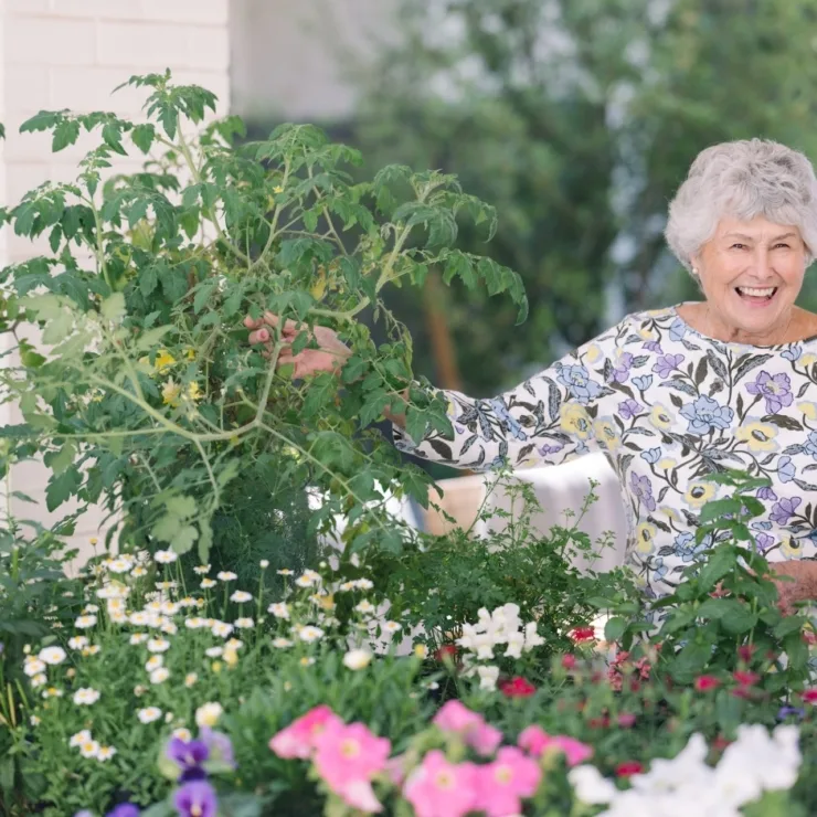 A joyful resident tends to vibrant flowers and plants, fostering a warm, nurturing community atmosphere.
