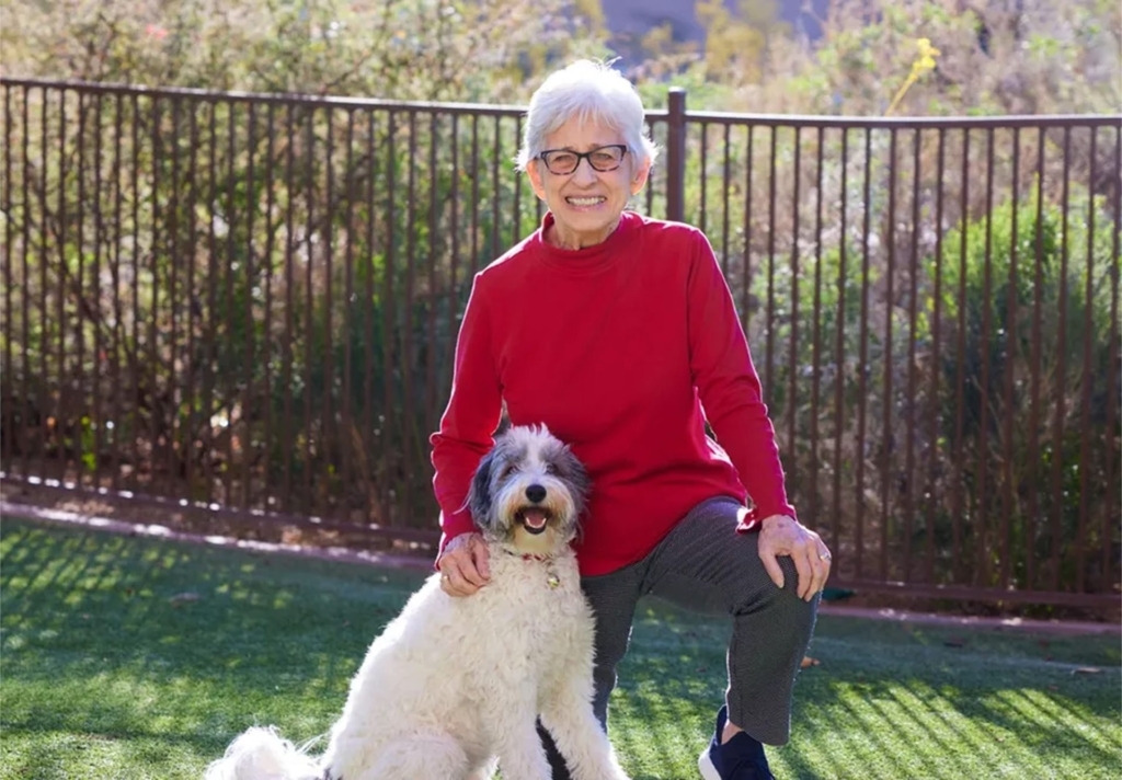 A cheerful resident enjoys quality time with a friendly dog in a vibrant, green outdoor space.