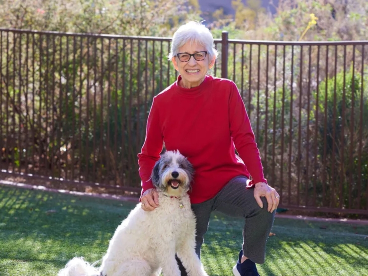 A cheerful resident enjoys quality time with a friendly dog in a vibrant, green outdoor space.